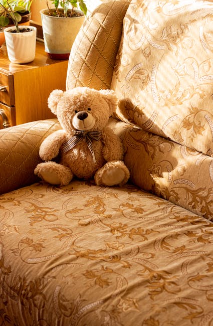 A beige fabric upholstered sofa positioned against a white wall with decorative molding in a well-lit living room. The sofa appears clean and plush, with two large seat cushions and matching back cush
